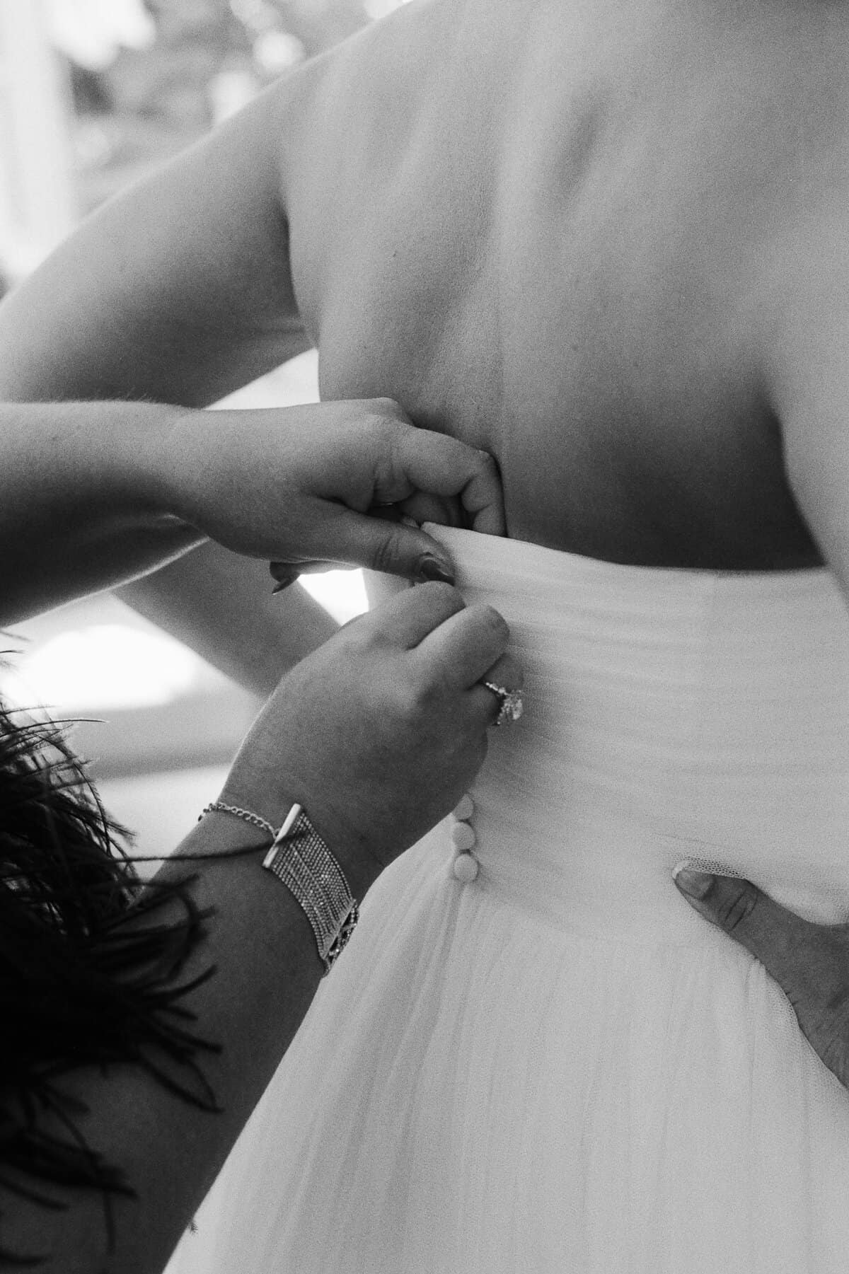 Close-up of a nantucket bride having the back buttons fastened on her strapless wedding dress, captured by a nantucket wedding photographer.