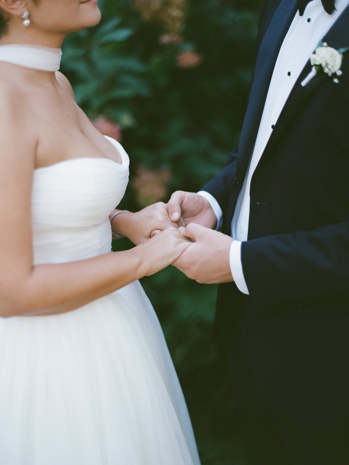 A bride and groom in formal wedding attire hold hands outdoors, captured in a timeless film photo by Nantucket Wedding Photographer Kaity Farrell. The bride wears a strapless white dress, and the groom is in a classic black tuxedo.
