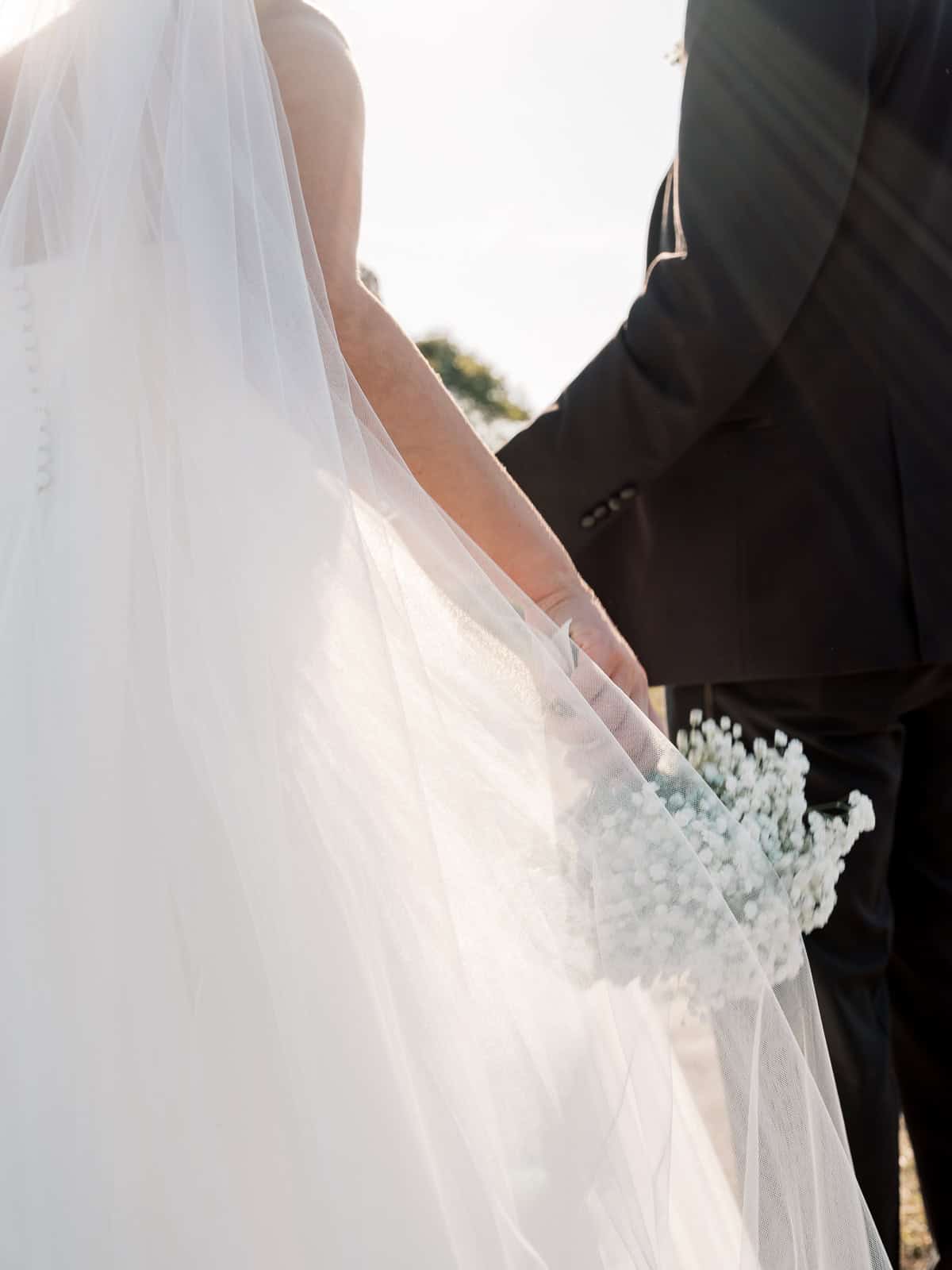 A bride and groom holding flowers, beautifully captured by Nantucket Wedding Photographer Kaity Farrell.