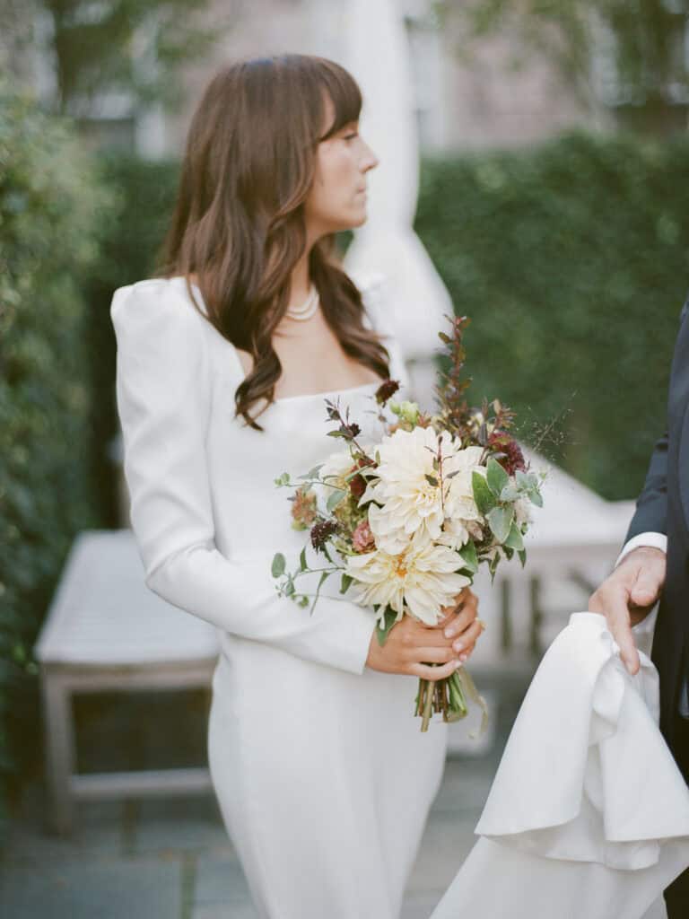 A woman in a white dress holds a bouquet of flowers, standing outdoors beside someone in formal attire, captured beautifully by Nantucket Wedding Photographer Kaity Farrell on film photo.
