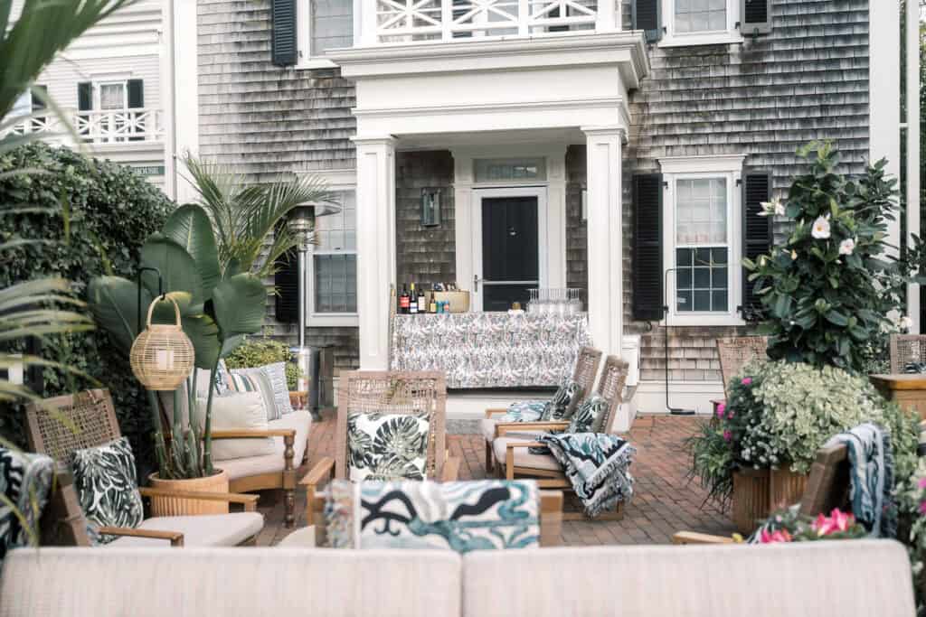Outdoor patio with wicker furniture, tropical cushions, lush greenery, and a bar setup in front at Faraway Nantucket hotel by Nantucket Wedding Photographer Kaity Farrell.