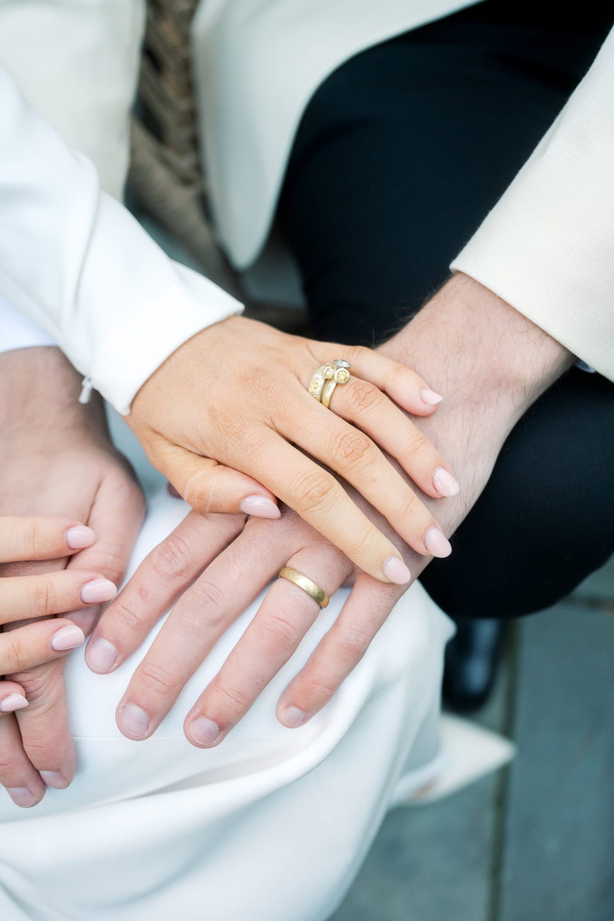 Close-up of a bride and groom resting their hands together, both wearing wedding bands and light-colored formal clothing. Captured by Nantucket Wedding Photographer Kaity Farrell.