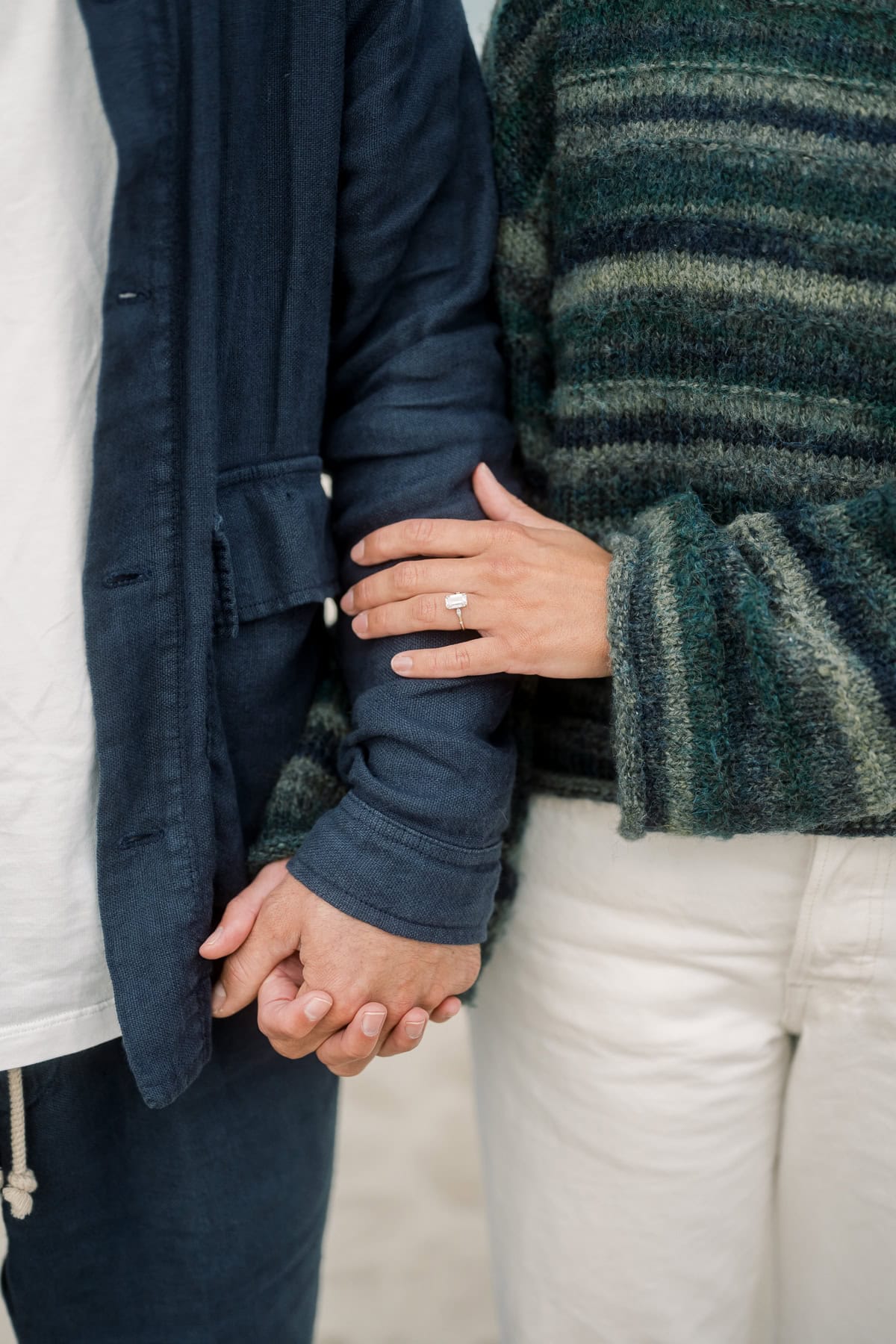 Two people stand side by side holding hands. One person’s arm is linked with the other’s, showing a ring on their finger. Both wear casual clothes, perfectly capturing an engagement photo session by Nantucket photographer Kaity Farrell.