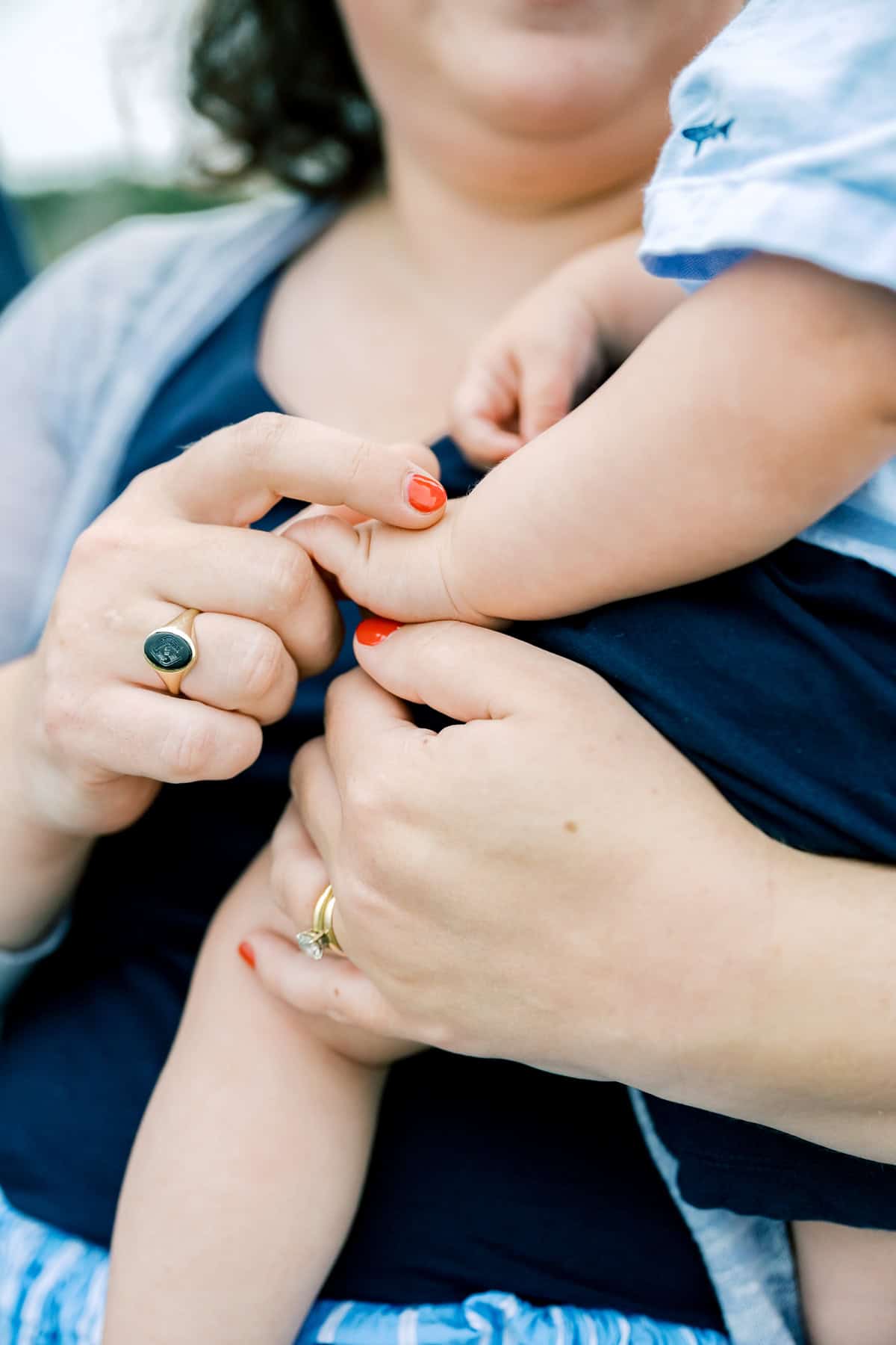 Close-up of a mother holding her baby; Nantucket family photographer Kaity Farrell captures the gentle grasp, rings, and red nail polish, with faces partially out of frame.