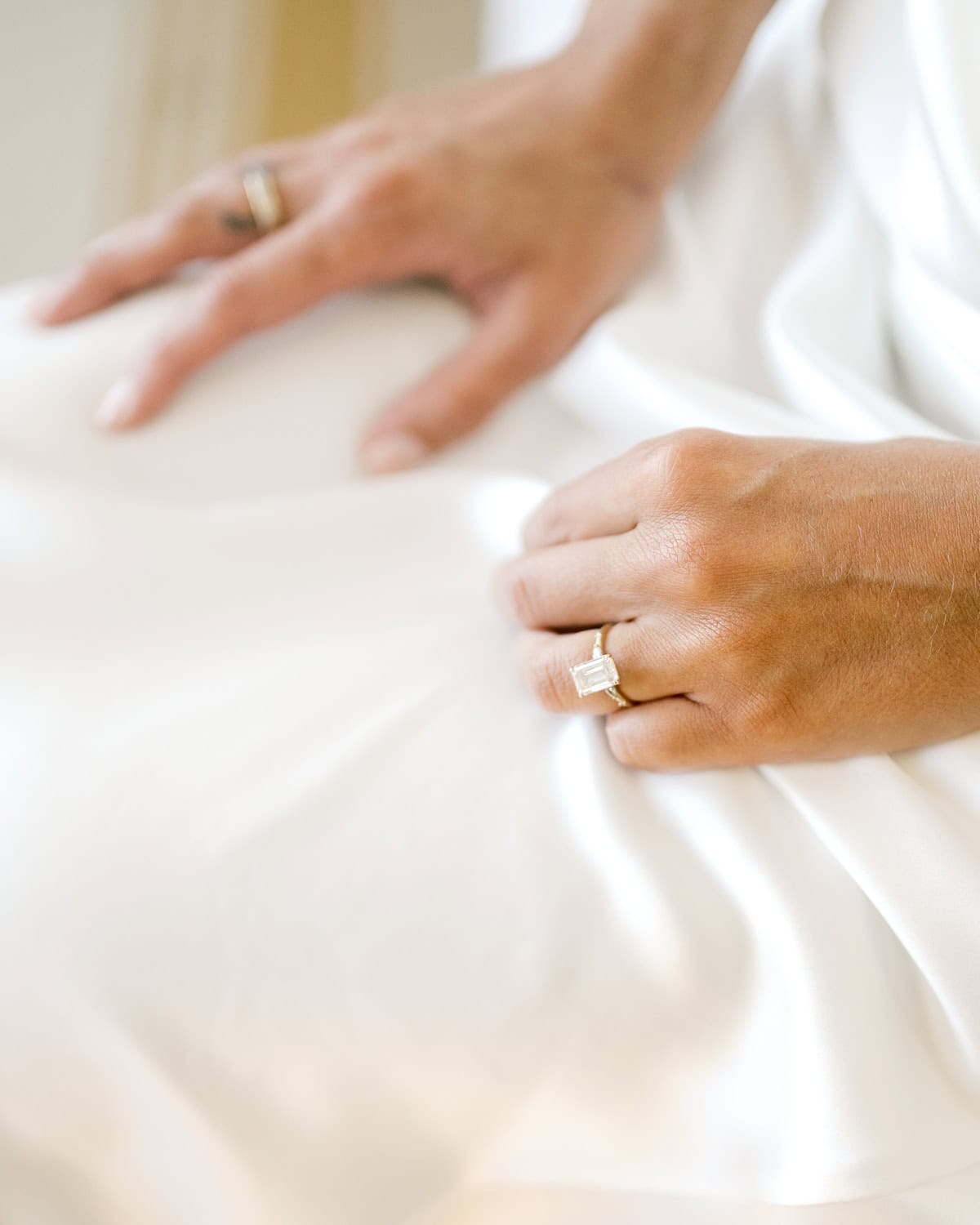 Close-up of a Nantucket bride's two hands resting on white fabric, both wearing rings, with a focus on a diamond engagement ring on the left hand. Captured by Nantucket Wedding Photographer Kaity Farrell.