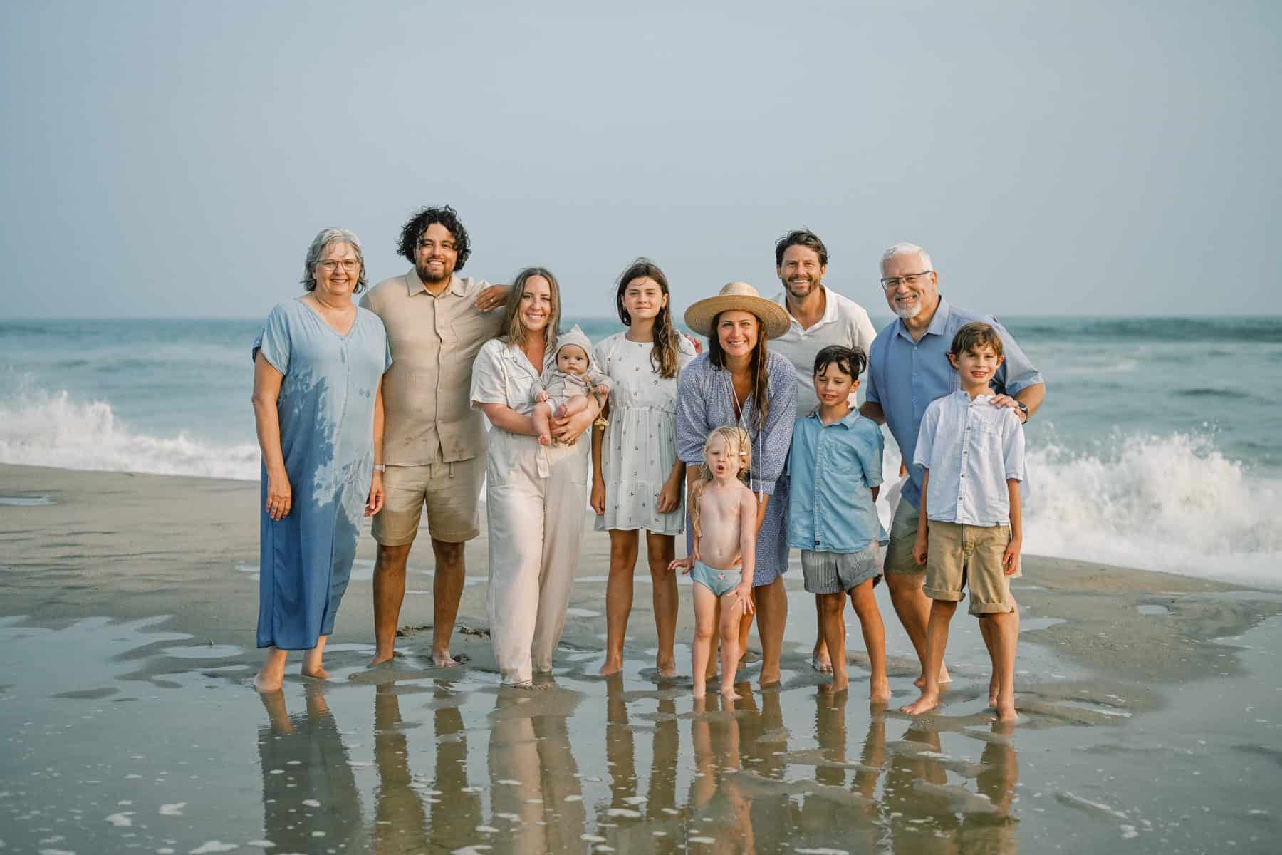 A multi-generational family stands together on a Nantucket beach with waves in the background, smiling for a group photo—capturing the warmth and connection of classic Nantucket family portraits.