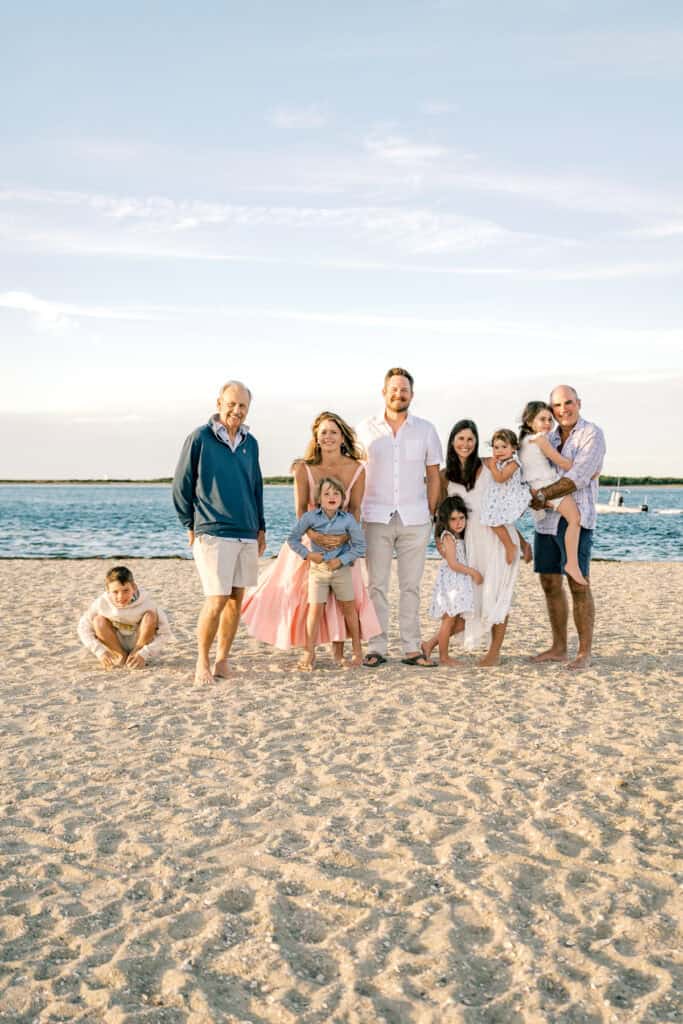 A multigenerational family poses together on a sandy Brant Point beach with the ocean in the background under a clear sky, captured beautifully by photographer Kaity Farrell.