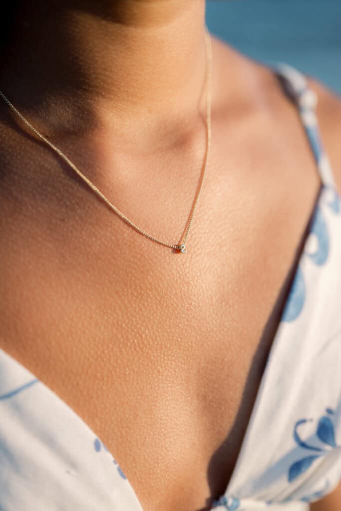 Close-up of a young woman wearing a delicate gold necklace with a small pendant, dressed in a white and blue patterned garment—captured by photographer Kaity Farrell for Nantucket senior portraits.